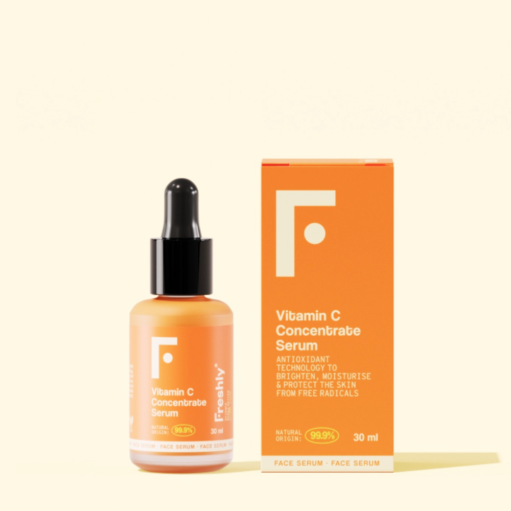 Um frasco e uma caixa de Freshly Sérum Concentrado de Vitamina C 30 ml são mostrados em um fundo claro. A embalagem laranja e branca destaca a proteção antioxidante contra o envelhecimento precoce, com detalhes do produto e logotipo visíveis.